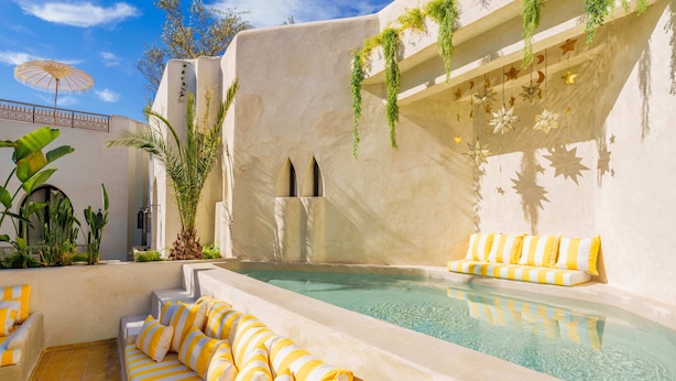 A pool area with a sofa, a sun umbrella, and a wall with hanging star decorations. - RIAD XO (Marrakech)