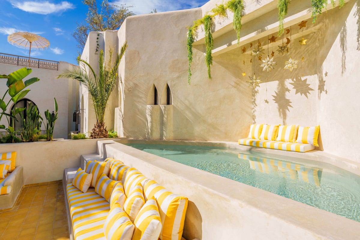 A pool area with a sofa, a sun umbrella, and a wall with hanging star decorations.