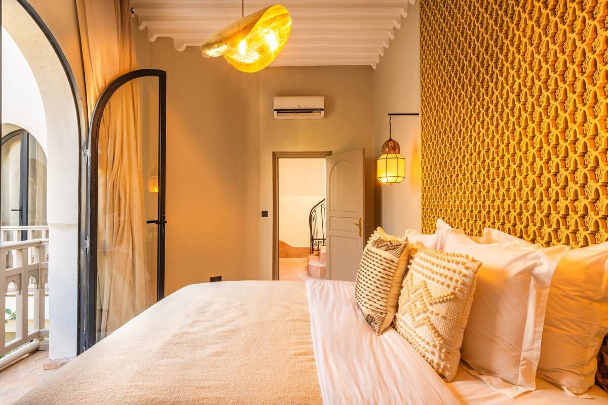A hotel room with a bed, a mirror, an air conditioning unit, a door, and a patterned wall.