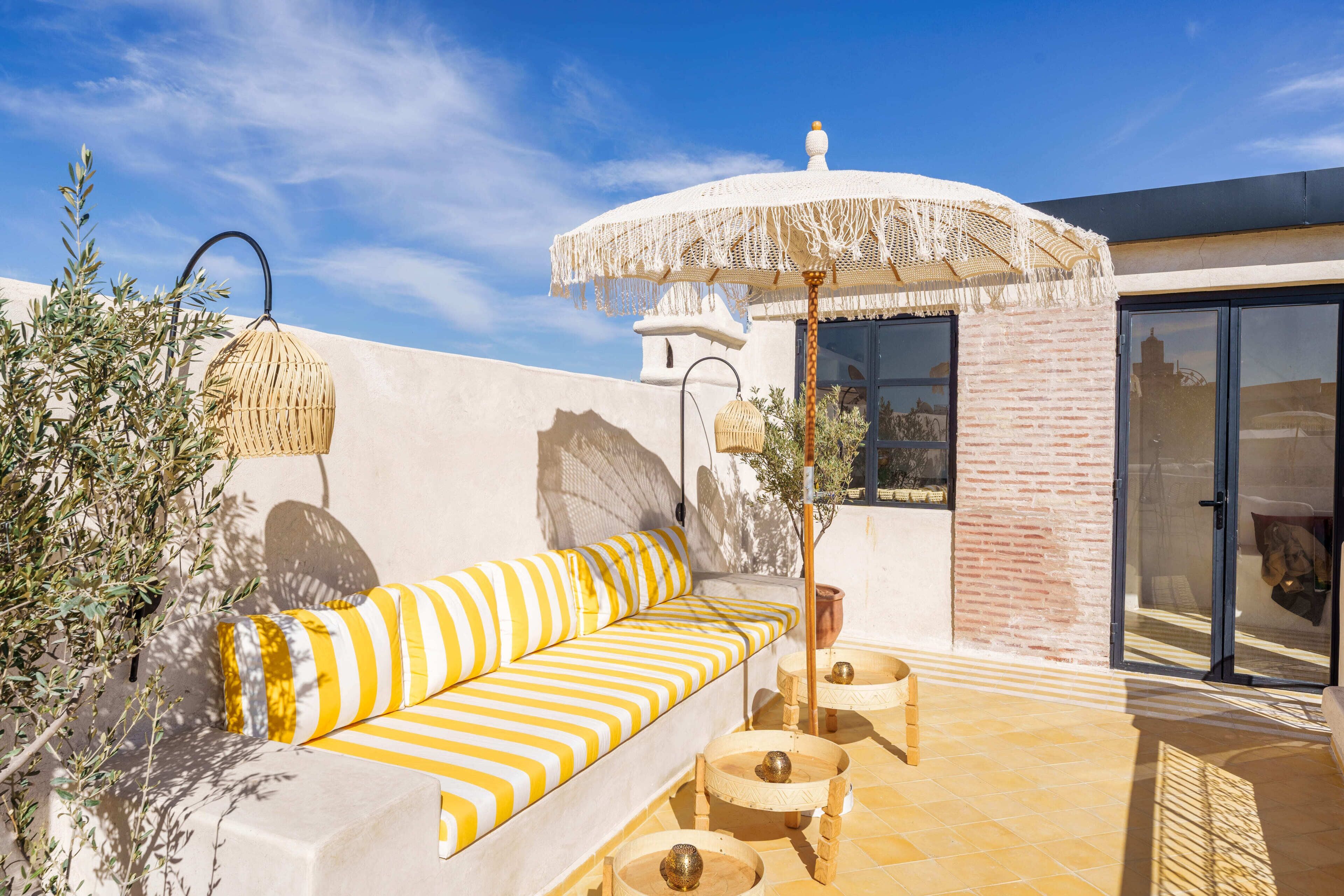A sunlit outdoor seating area with a striped sofa, a woven umbrella, and a small table.