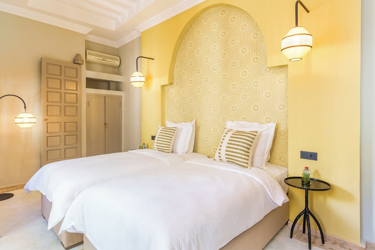 A bedroom with a large bed, two bedside lamps, a small table, and a decorative wall pattern.