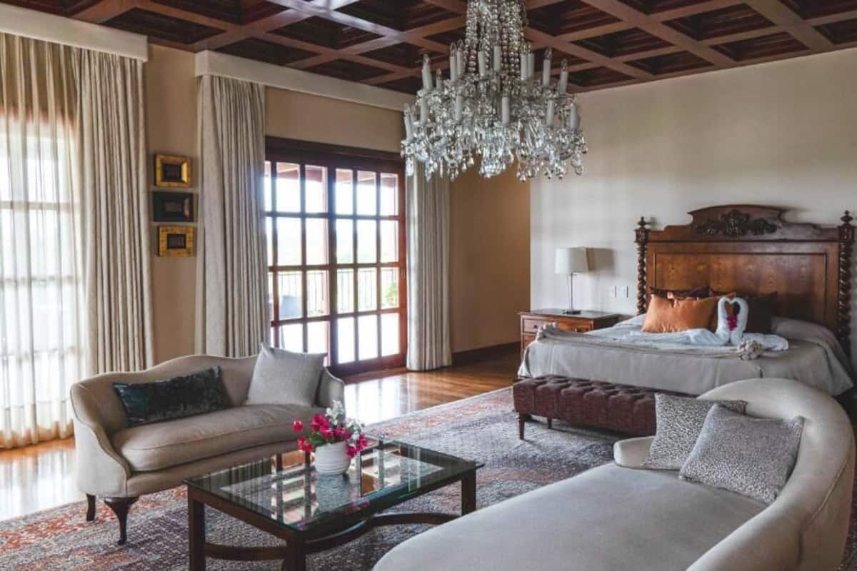 A spacious bedroom with a large bed, two bedside tables, a chandelier, and a view through a window.