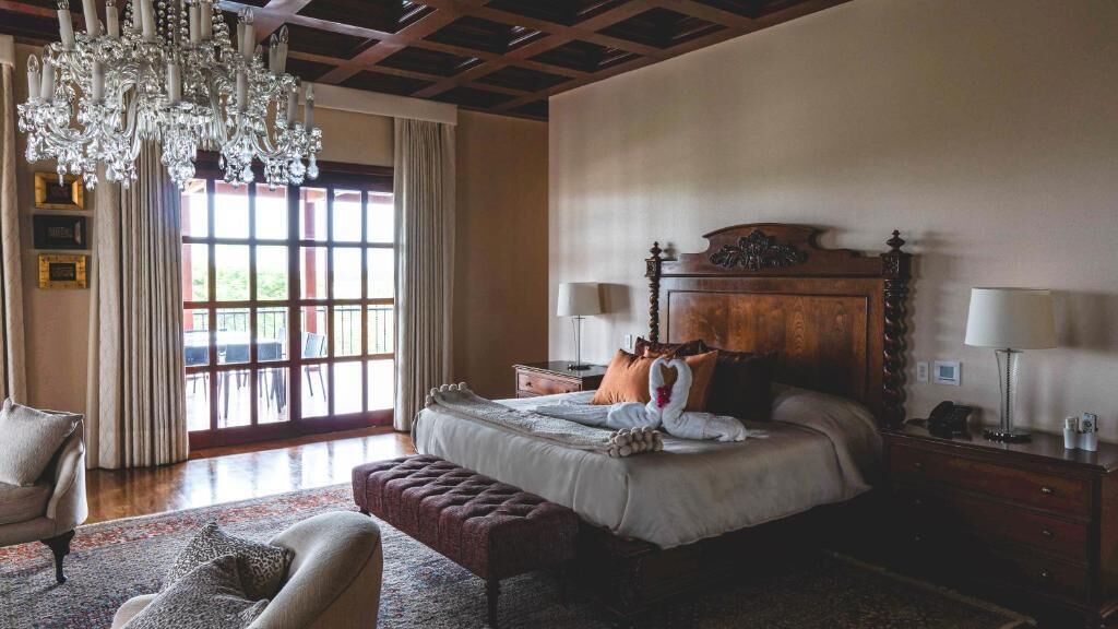 A spacious bedroom with a large bed, a chandelier, and a view through a window.
