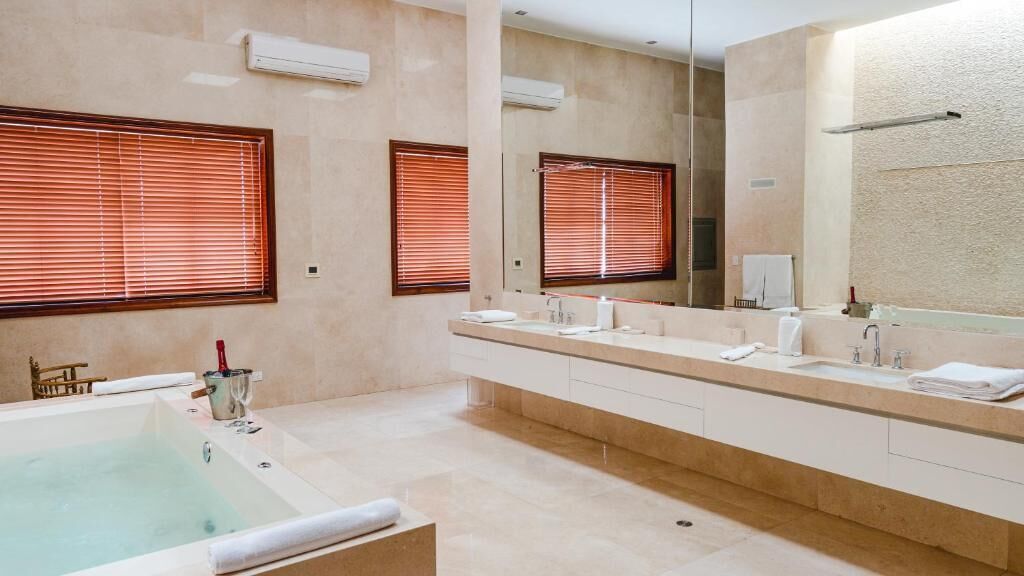 Un bagno moderno con una vasca, due lavandini, uno specchio grande e persiane in legno.