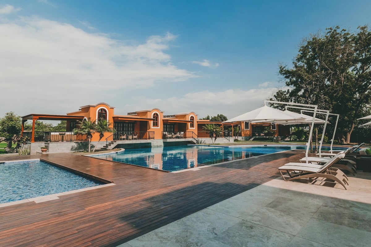 A swimming pool area with a wooden deck, lounge chairs, and a building with arched windows.
