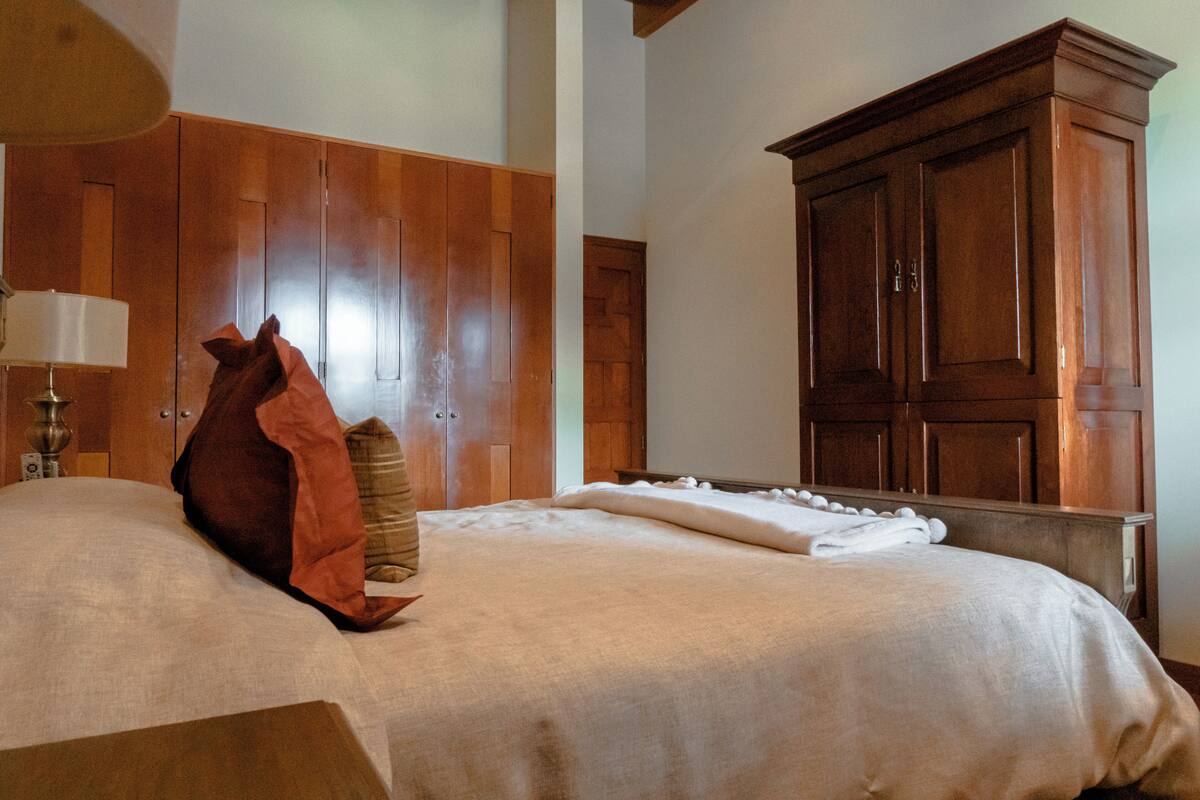 A hotel room with a large wooden wardrobe, a bed with white linens, and a lamp on a bedside table.