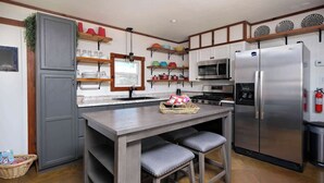A modern kitchen with grey cabinets, a stainless steel refrigerator, a microwave, and a gas stove. There are two bar stools at the island and a basket of bread on the counter. - 3BR Sleep 6 PALO DURO CANYON Bunker Cabin Pet OK (Canyon)
