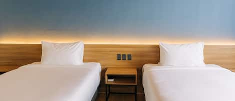 Habitación de hotel con dos camas individuales, un cabecero de madera, una mesita de noche con lámpara y vistas al cielo.
