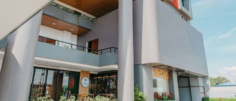 Um edifício moderno com um café no andar térreo, várias varandas e uma faixa vertical vermelha marcante.