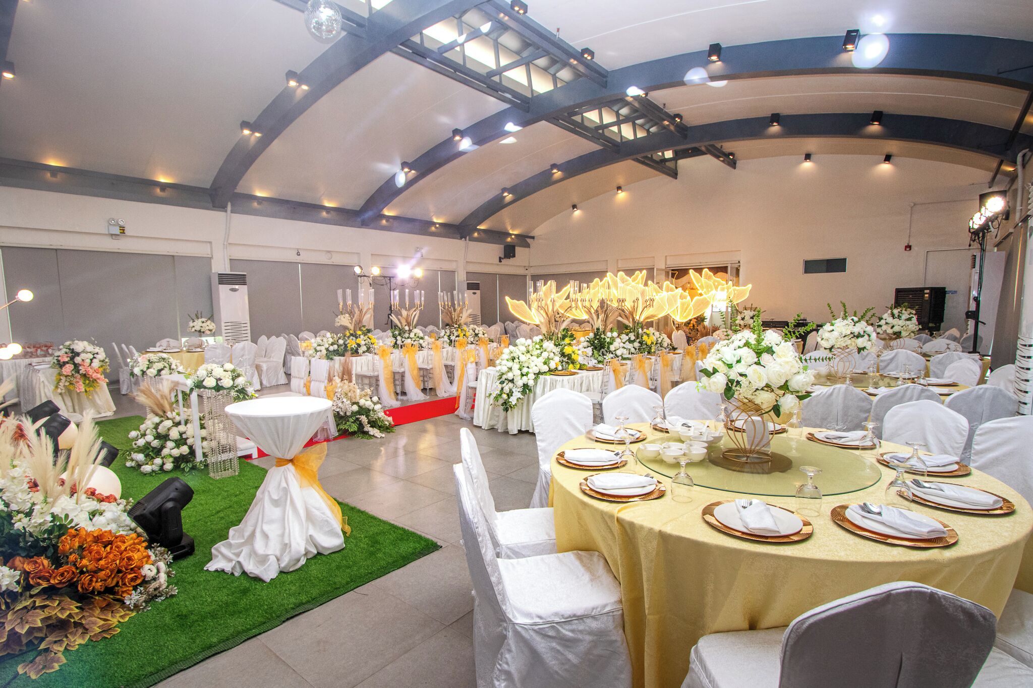 A banquet hall with round tables set for dining, surrounded by white chairs and floral centerpieces.
