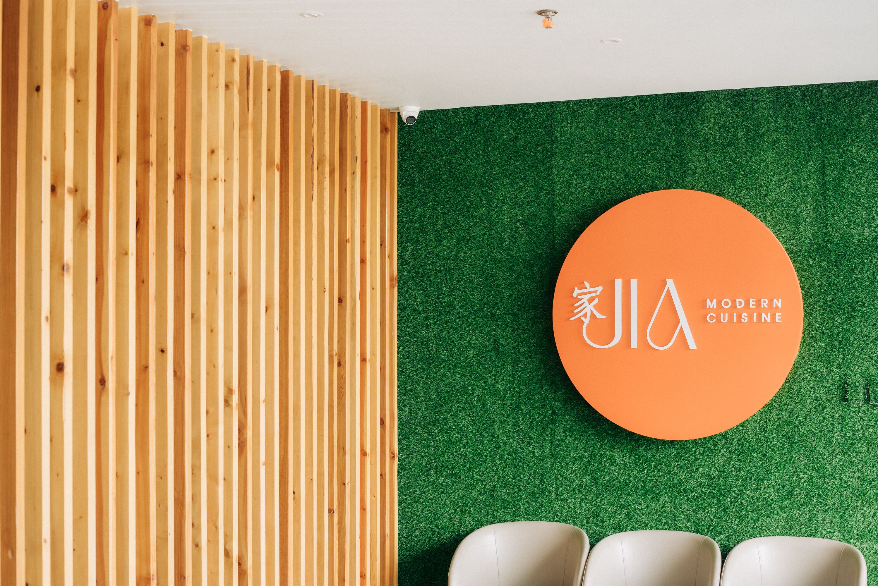 Ein modernes Interieur mit einer Wand aus Holzlamellen, einer grünen Wand mit einem runden, orangefarbenen Schild und drei weißen Stühlen.