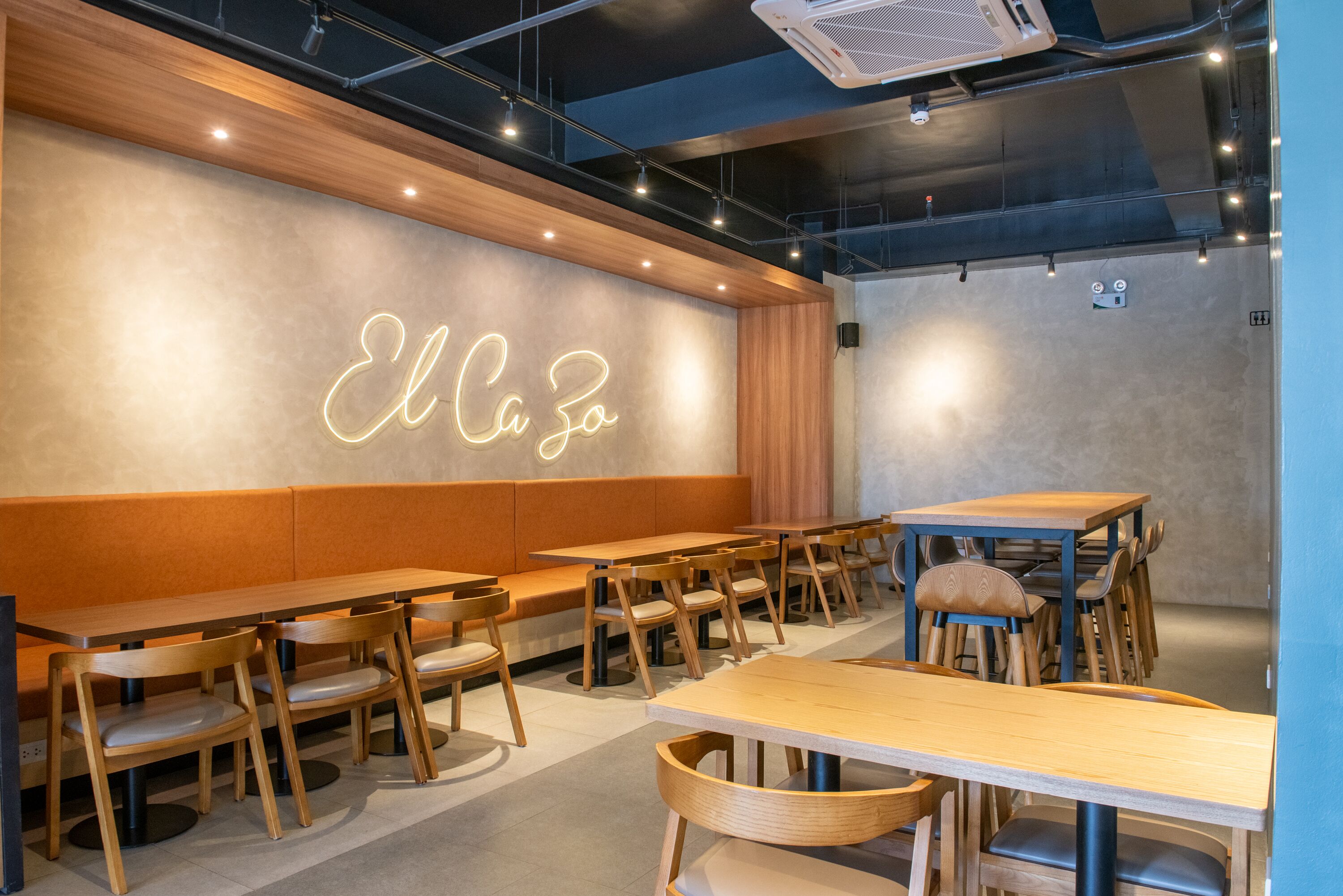 A modern restaurant interior with wooden tables and benches, a neon sign, and recessed lighting.