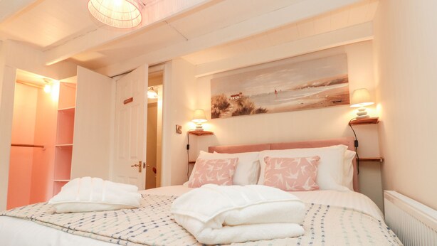 A neatly made bed with pillows and folded towels, a painting on the wall, and a lamp on a bedside table. - Red Grouse Cottage (Guisborough)