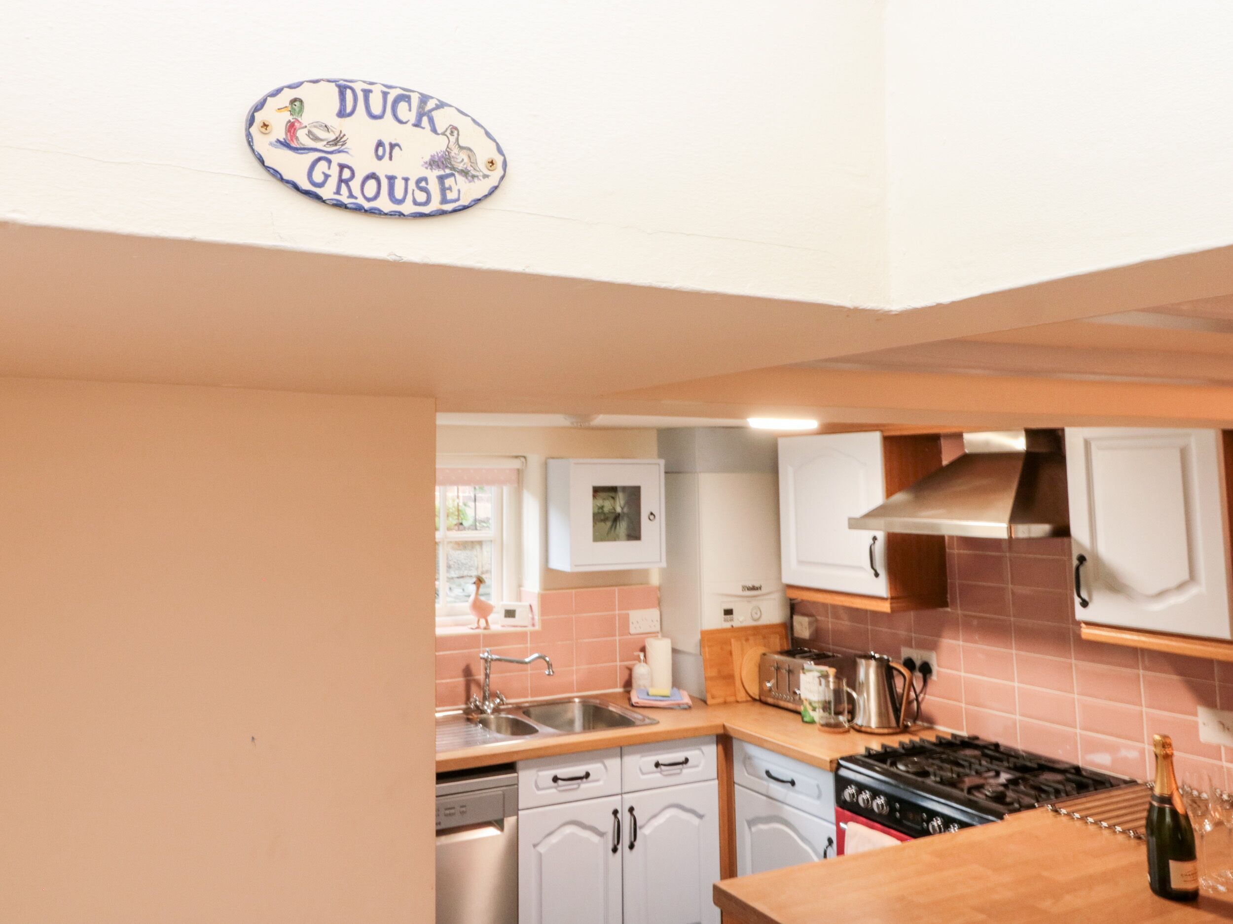 Een keuken met witte kastjes, een fornuis en een spoelbak. Boven de spoelbak hangt een bordje met de tekst 'Duck or Grouse'.
