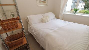 A neatly arranged bedroom with a bed, a window with a view of houses, and a metal rack with baskets.