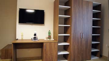 A room with a wooden desk, a flat-screen TV, and a large wardrobe with multiple shelves.