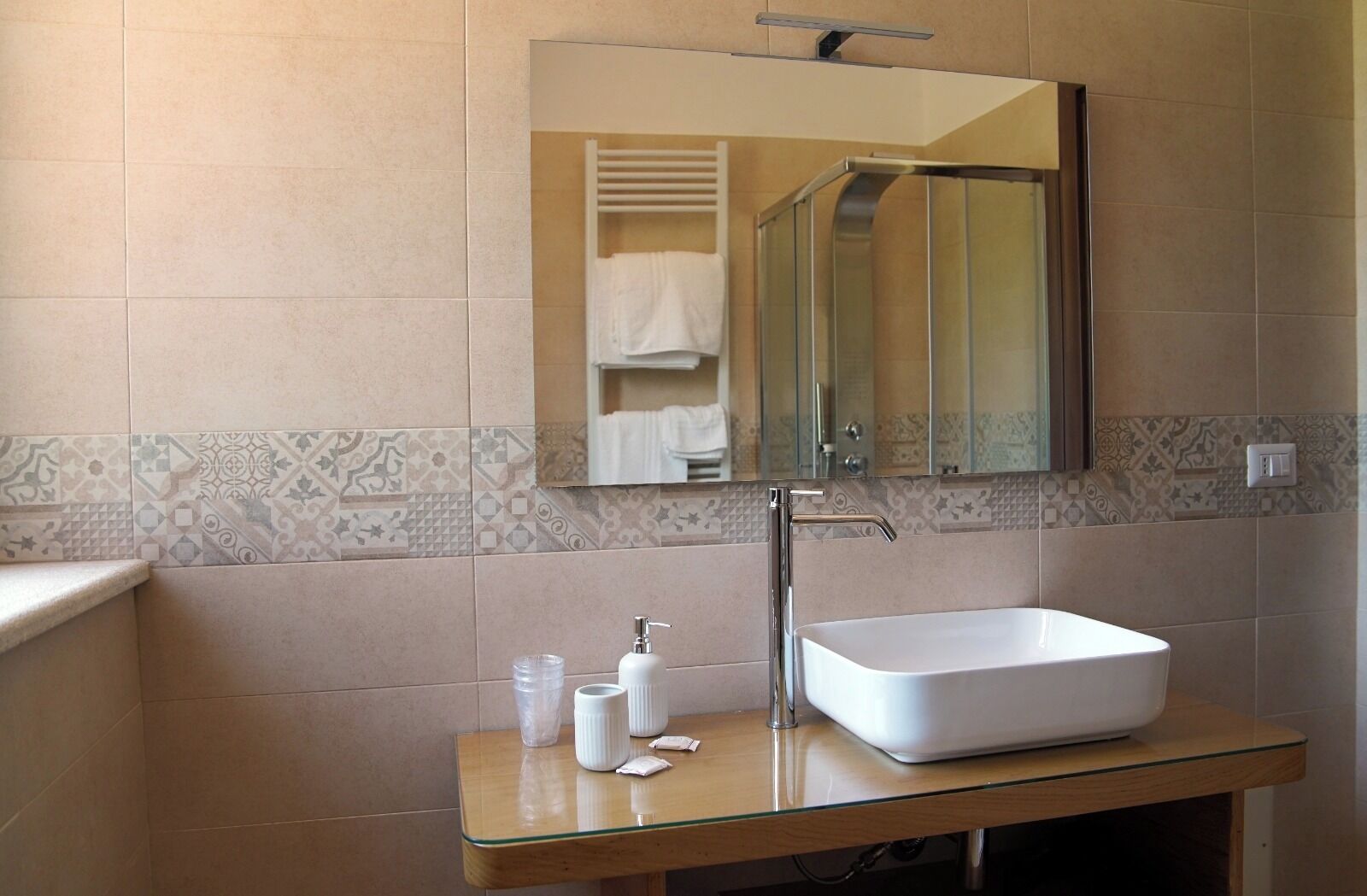 A bathroom with a glass-top sink, a mirror, and a towel rack.