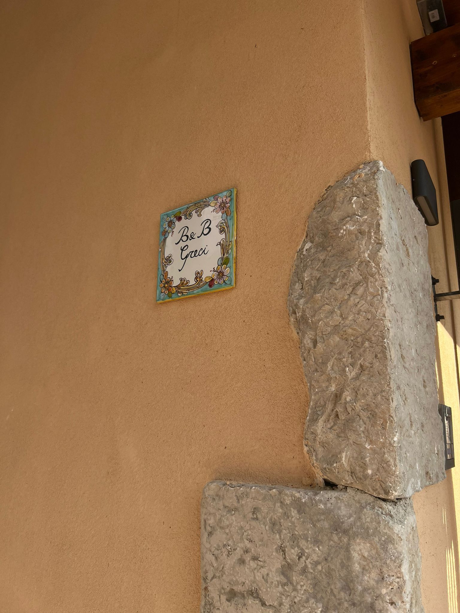 Un mur orné d’une enseigne décorative sur laquelle on peut lire « B&B Graci », ainsi que deux gros rochers.