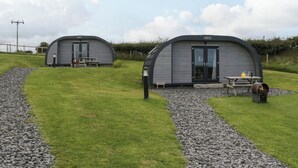 Two modern, semi-circular, grey-roofed cottages with a picnic table and a small garden area in front. - Forest (Dalton-in-Furness)