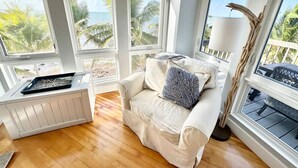 A room with large windows, a white cushioned chair, a small white table, and a lamp.