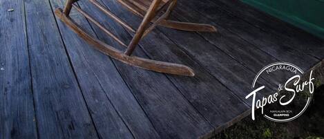 Une chaise à bascule en bois sur une véranda, avec un mur vert et rouge, un plafond en bois et une petite lanterne jaune.