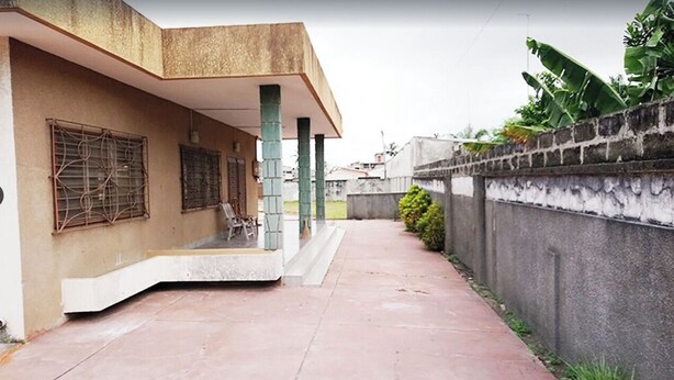 Un edificio con un porche cubierto, un sendero de concreto y un muro de ladrillo con vegetación.