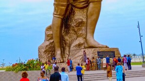 Una estatua de bronce de gran tamaño muestra a un guerrero sosteniendo una espada, sobre un pedestal con una placa.