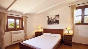 A bedroom with a large bed, two bedside tables with lamps, a radiator, and a window with curtains. - Villa Poley (IB)