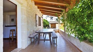A covered patio with a table and benches, stone walls, and a wooden ceiling. - Villa Poley (IB)