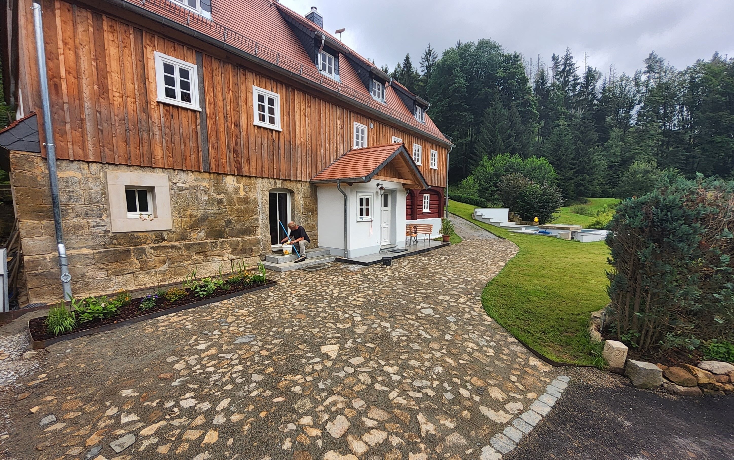 A stone-paved courtyard with a wooden building, a stone wall, and a small garden area.