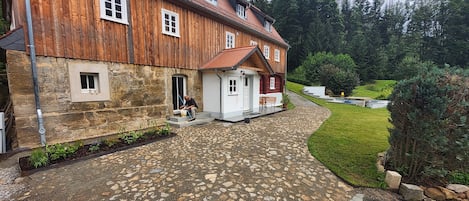 A stone-paved courtyard with a wooden building, a stone wall, and a small garden area.