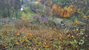 Un paysage rural avec une vallée, des arbres aux couleurs automnales et une petite maison.