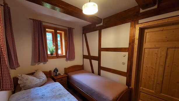 A bedroom with a bed, a nightstand, a lamp, and a window with curtains. - Peace and relaxation in Saxon Switzerland (Sebnitz)