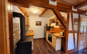 A kitchen with wooden beams, a stone wall, and a black stove. - Peace and relaxation in Saxon Switzerland (Sebnitz)