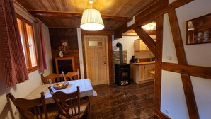 A rustic interior with a dining table, chairs, a wooden ceiling, a stone fireplace, and a kitchen area. - Peace and relaxation in Saxon Switzerland (Sebnitz)