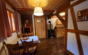 A rustic interior with a dining table, chairs, a wooden ceiling, a stone fireplace, and a kitchen area. - Peace and relaxation in Saxon Switzerland (Sebnitz)