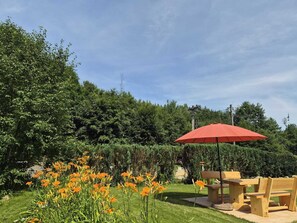 A garden with a wooden table and chairs, a red umbrella, and orange flowers. - Peace and Relaxation in Saxon Switzerland (Sebnitz)