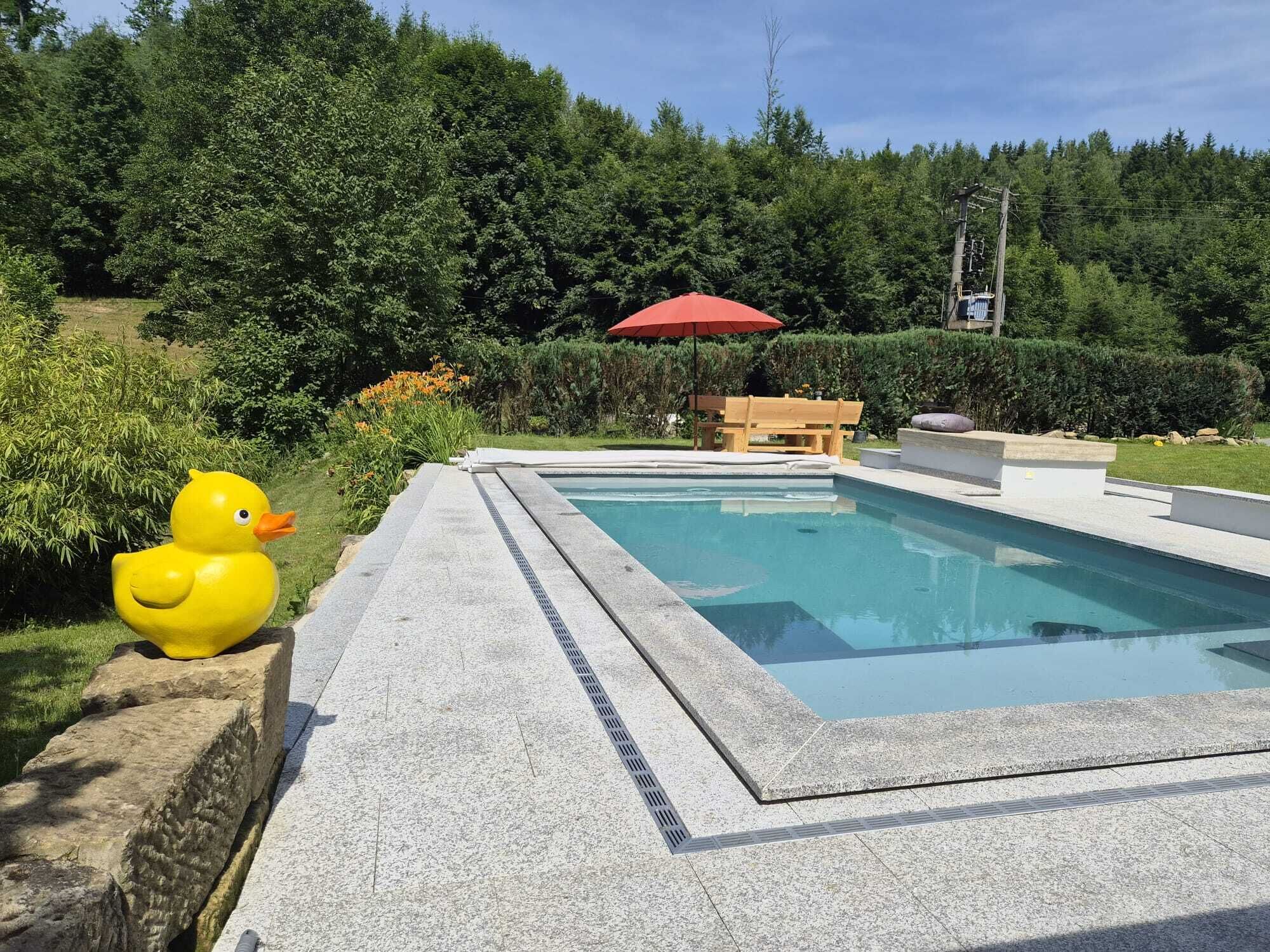 A swimming pool with a wooden bench and a red umbrella.