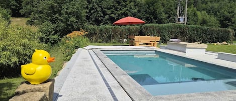 A swimming pool with a wooden bench and a red umbrella.