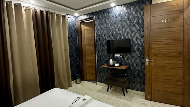 A hotel room with a bed, a ceiling fan, a TV on a wooden stand, and a wardrobe with the number 203. - VIKRANT RESIDENCY 59 (Gurugram)