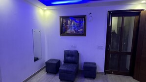 A room with a large mirror, a framed painting, and three ottomans. - VIKRANT RESIDENCY 59 (Gurugram)