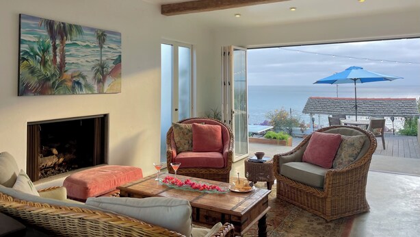 A cozy living room with a fireplace, wicker furniture, and a view of the ocean. - 100' of Ocean Frontage at Moonlight Beach (Encinitas)