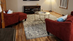 Uma sala de estar com televisão de tela plana, sofás vermelhos, uma mesa de centro e um tapete estampado.