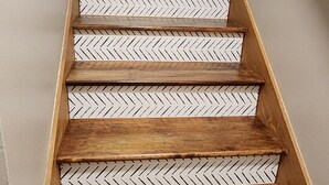 Uma escadaria de madeira com padrão herringbone nos degraus e corrimão de metal.