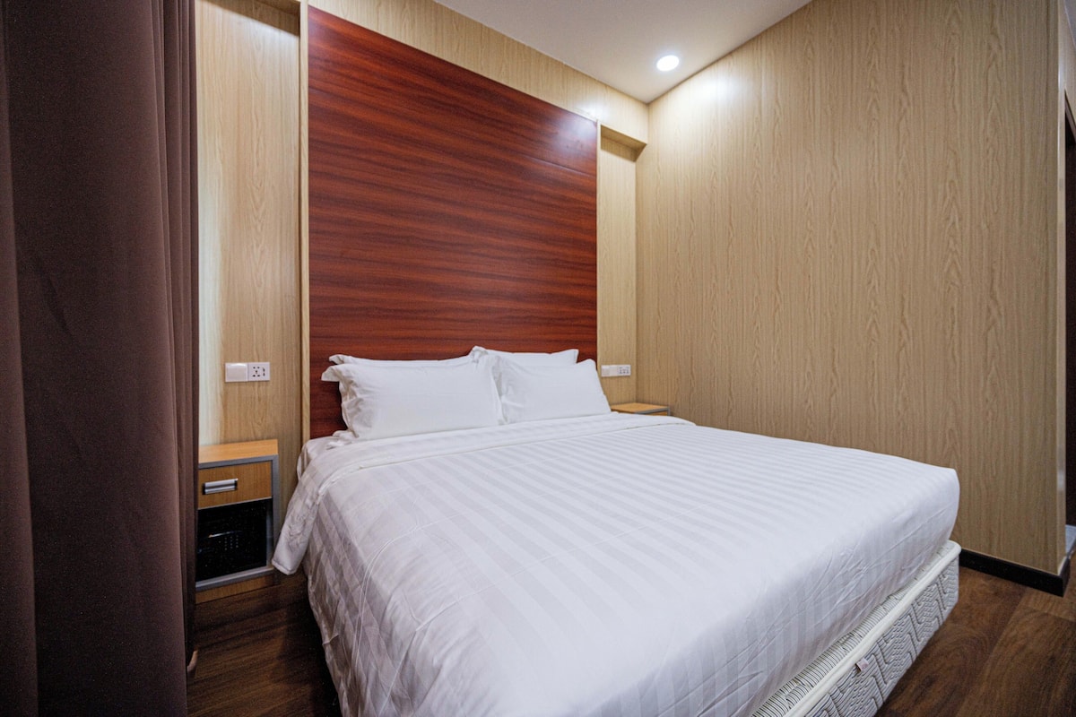 A neatly made bed with white linens in a hotel room with wooden paneling and a wooden headboard.