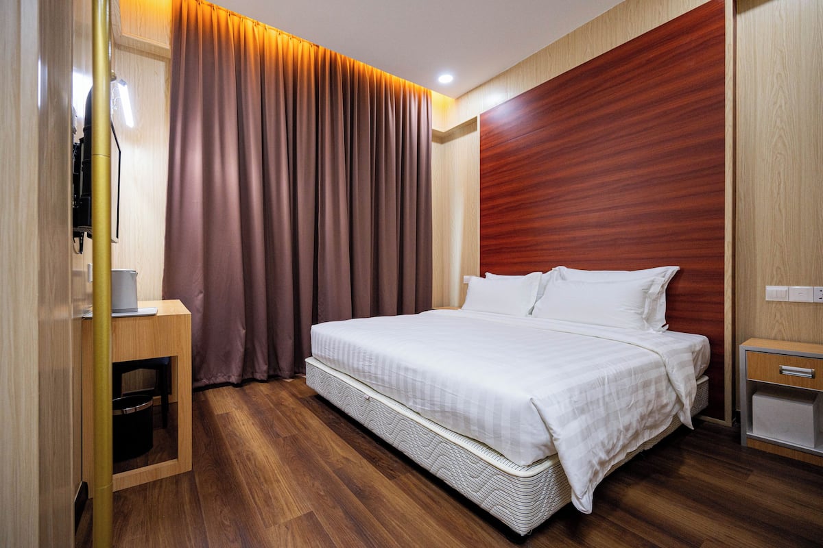 A modern hotel room with a large bed, wooden flooring, a wooden headboard, a bedside table, and a built-in TV.