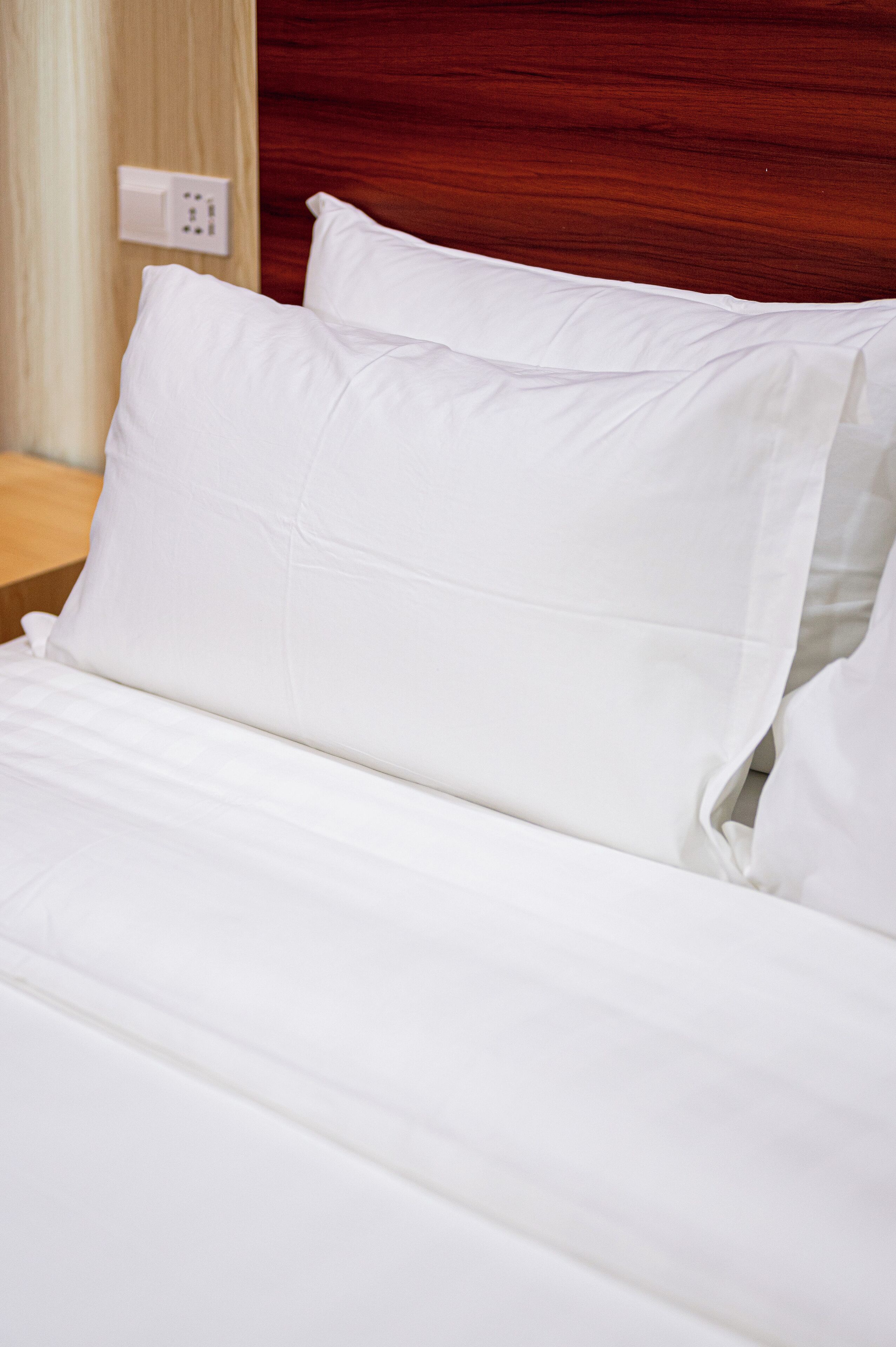 A neatly made bed with white linens and a wooden headboard.