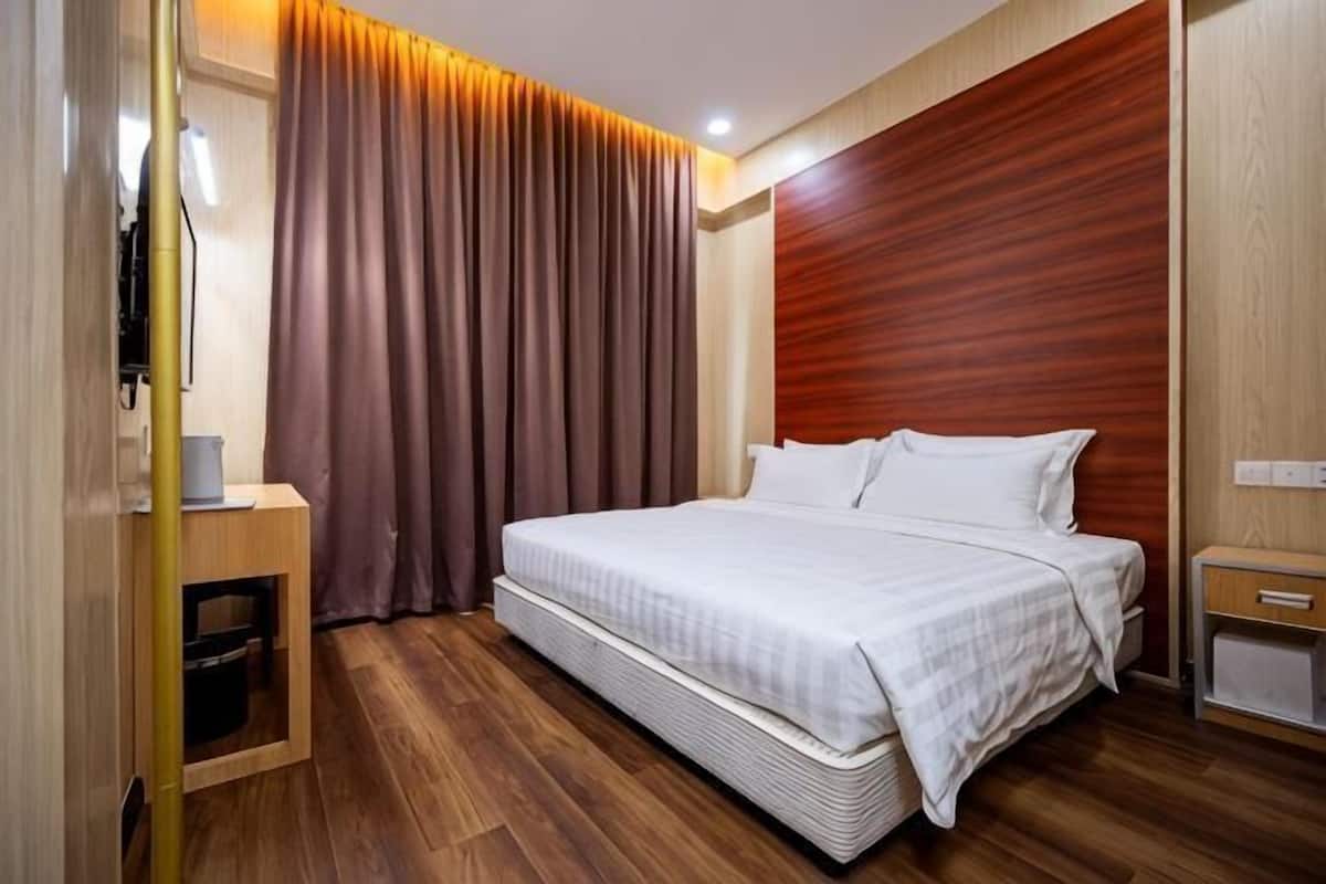 A hotel room with a large bed, wooden flooring, a wooden headboard, a bedside table, and a curtain.