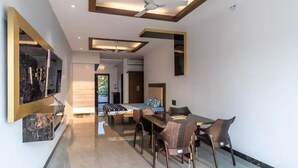 A modern living room with a dining area, a ceiling fan, and a large mirror. - Raj Sea Front Beach Resort 203 (Mangaluru)