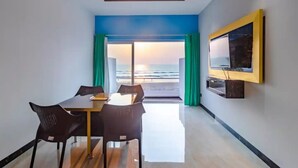 A modern room with a dining table and chairs, a ceiling fan, a large window with curtains, and a mounted television. - Raj Sea Front Beach Resort 203 (Mangaluru)